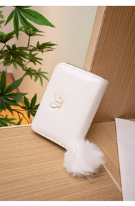 Gros plan d'un porte-monnaie blanc avec papillon doré et breloque boule de poils douce
