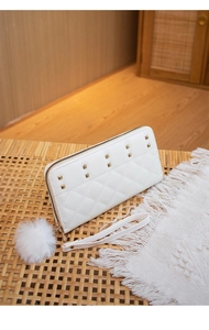 Detail of white quilted wallet featuring gold square studs and a plush pompom charm