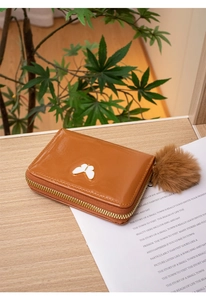 Détail d'un mini porte-monnaie en cuir verni marron avec papillon et pompon en peluche