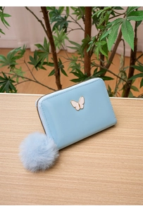 Détail d'un porte-monnaie bleu clair en simili cuir avec logo papillon et pompon pelucheux