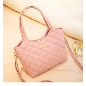Detail of pink quilted handbag featuring gold metal bar and adjustable strap on soft decor