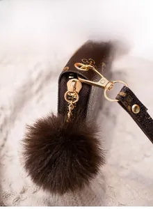 Close-up of brown patterned wallet featuring gold hardware and dark brown pompom charm