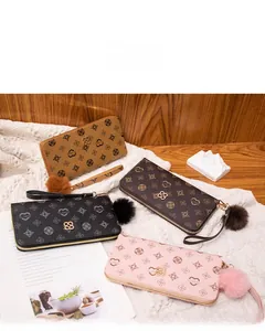 Flat lay of long floral print wallets in four colors with pompom charms and wristlets