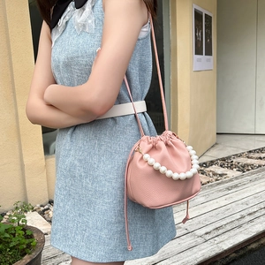 Chic pink drawstring bucket bag with pearl handle and lychee texture worn by model