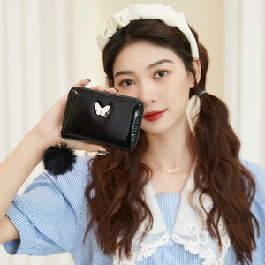 Portefeuille en cuir verni noir avec décor papillon et pompon tenu par un mannequin