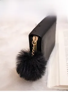 Dettaglio del portafoglio in pelle nera con cuciture a zigzag e grande pompon in ecopelliccia