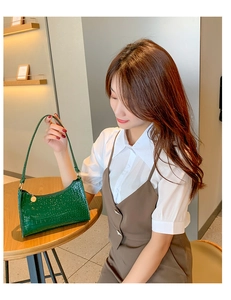 Detailed view of dark green faux crocodile texture handbag with gold zipper charm