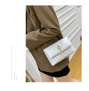 Détail d'un sac à bandoulière blanc matelassé avec pendentif couronne dorée et chaîne