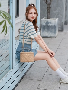 Close-up of beige quilted bucket bag with top handle and gold zipper on a wooden bench