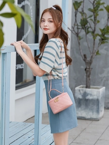 Detail of pink quilted bucket bag with gold zipper and strap against a garden backdrop