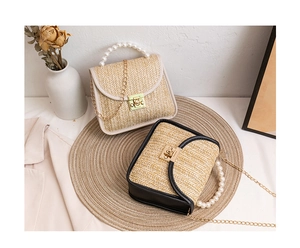 Detail of woven straw handbag featuring a pearl bead handle and golden metal turn lock