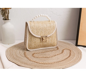 Detail of woven straw handbag featuring pearl top handle and golden chain strap