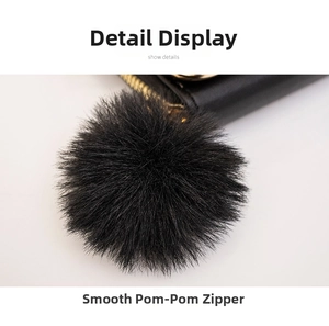 Detail of a quilted crossbody bag featuring a gold zipper and a smooth black faux fur pompom