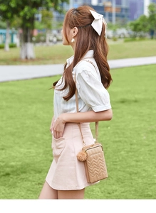 Close-up of khaki quilted leather phone bag with V-shaped stitching and plush charm