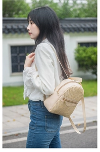 Detail of a beige woven mini backpack with gold zippers shown on a model outdoors
