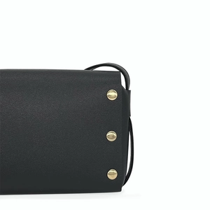 Détail d'un sac en cuir noir avec trois rivets dorés sur le panneau latéral