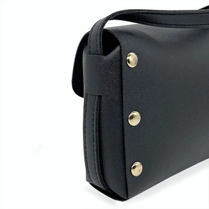 Détail de la texture cuir noir grainé et des rivets métalliques dorés sur le sac à bandoulière