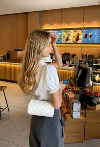White quilted cylinder chain bag worn by model in a modern cafe setting
