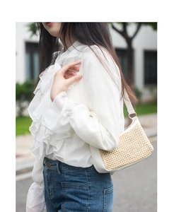 Détail du sac à bandoulière en paille tissée avec garniture en cuir blanc et dorures