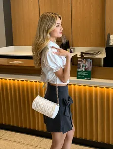 White quilted cylinder bag with gold chain strap shown on a model in a cafe setting