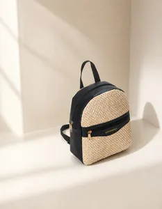Detail of woven straw and black leather backpack with gold fashion logo and metal zippers