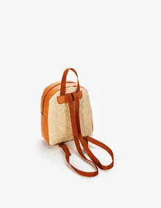 Detail of woven straw mini backpack showing adjustable straps and brown leather patchwork