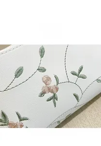 Detailed macro view of delicate floral embroidery on white faux leather shoulder bag