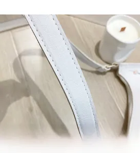 Close-up of white lychee leather shoulder strap with stitching and flower embroidery