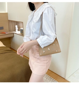 Detail view of tan embroidered shoulder bag with floral lace patterns on a model's outfit