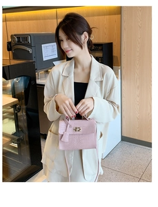 Detailed view of pink croc-embossed handbag with gold hardware on a wooden table