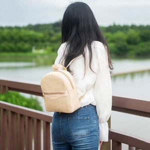 Mini woven straw backpack with beige leather trim shown on model in outdoor setting