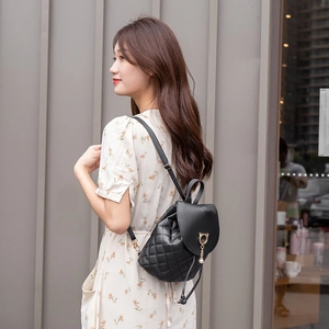 Black quilted mini backpack with pearl cat pendant shown on a model outdoors
