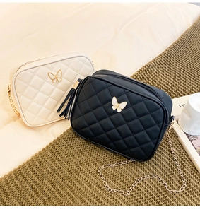 Detail of quilted crossbody bag with gold chain strap, butterfly hardware, and tassel