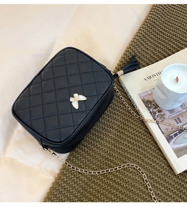 Detail view of black quilted crossbody bag featuring a white butterfly buckle and tassel