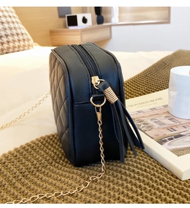 Detail view of black quilted crossbody bag with tassel charm and gold chain strap