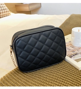 Close-up of black quilted shoulder bag with golden chain strap on a white bedding