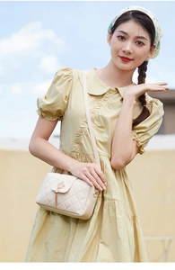 Détail du sac bandoulière beige matelassé avec fermoir couronne dorée et pompon sur robe