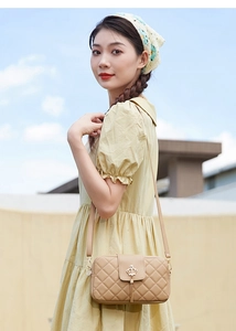 Détail du sac bandoulière beige matelassé avec ornement couronne dorée et pompon en métal