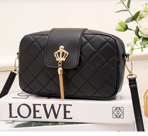 Vue détaillée d'un sac matelassé noir avec boucle couronne dorée et pompon sur des livres