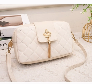 Détail du sac bandoulière beige avec matelassage en losanges et pompon couronne dorée