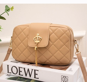 Détail d'un sac bandoulière beige matelassé avec couronne dorée et pompon sur livre