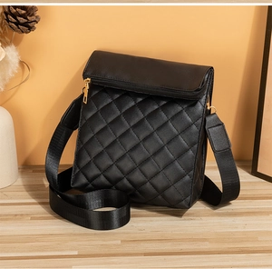 Détail du sac bandoulière matelassé noir avec zip doré sur une surface en bois