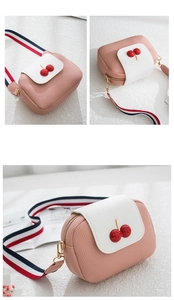 Detail view of pink crossbody bag with 3D cherry decor and striped woven strap