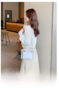 Detail of white PVC handbag featuring acrylic ring handle and gold chain strap in cafe setting