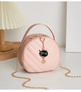 Detail of pink round quilted handbag featuring a golden cat pendant and chain strap