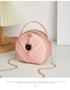 Close-up of pink quilted mini bag with black cat head pendant and golden chain strap