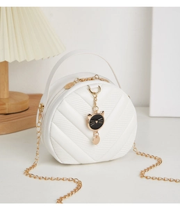 Close-up of white round crossbody bag with V-quilted faux leather and a cat-shaped charm