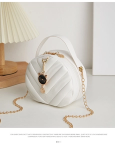 Detail of white quilted round crossbody bag with gold chain and cat charm in a cozy setting