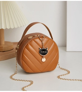 Close-up of brown quilted crossbody bag with golden chain and black cat pendant charm