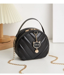 Detail of black round handbag featuring V-shaped quilting and a gold cat charm